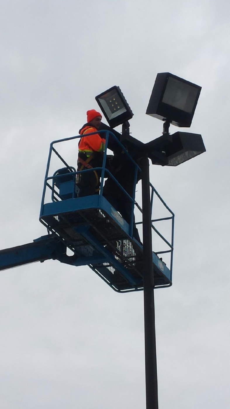 Electrician in an aerial lift servicing LED parking lot pole lights